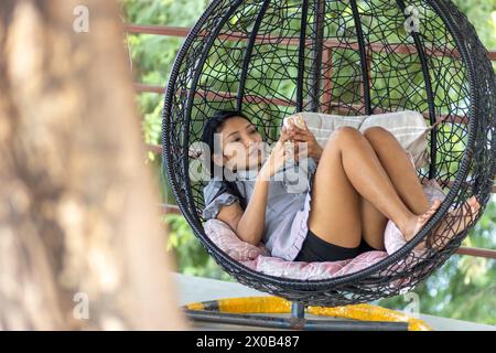 Une jeune femme se détend dans une chaise suspendue dans le jardin Banque D'Images