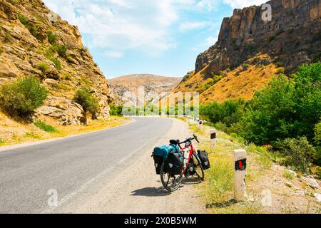 Chargé de sacs rouge vélo se tient sur le bord de la route entouré par la campagne en arménie, montagnes du caucase. Vacances à vélo. Banque D'Images