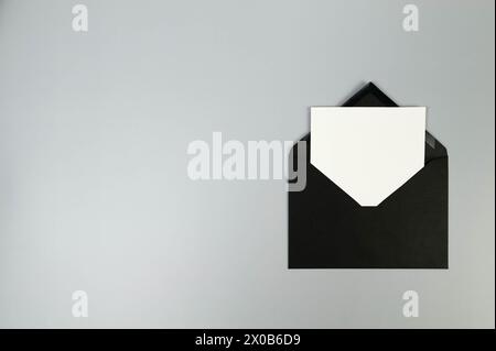 Vue de dessus de l'enveloppe noire, carte blanche sur fond gris. Post pose à plat. Copier l'espace. Banque D'Images
