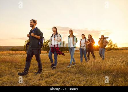 Groupe de touristes heureux avec des sacs à dos marchant à travers un champ lors d'une randonnée Banque D'Images