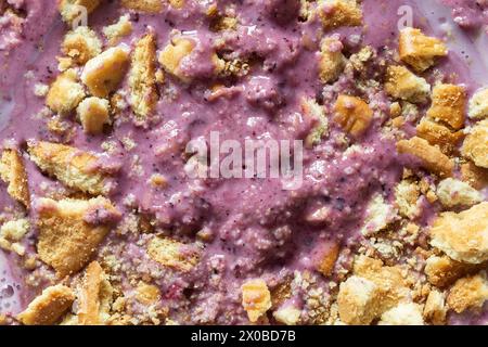 Vue aérienne d'une texture crémeuse d'un bol de smoothie aux baies mélangées violettes, saupoudrée d'une couche de biscuits dorés écrasés créant un attrait visuel Banque D'Images