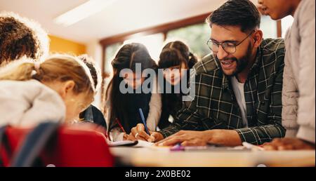 Un éducateur d'école primaire enseigne l'art à un groupe d'élèves de sexe masculin et féminin dans une salle de classe. La classe des élèves de l'école primaire prête attention à th Banque D'Images