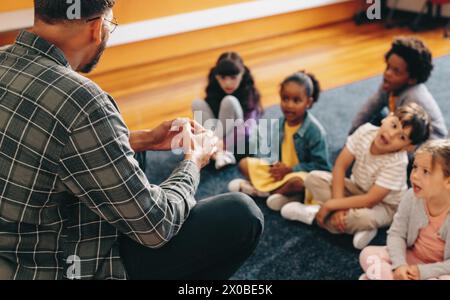 Éducateur enseigne une classe d'école primaire. Homme parlant devant un groupe d'enfants. Enseignant masculin donnant une leçon verbale de base, il enseigne aux enfants t Banque D'Images