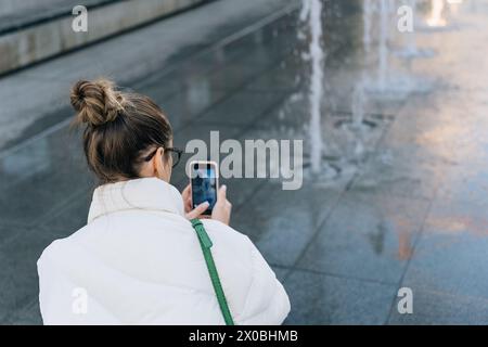 Femme prenant des photos de la fontaine avec le téléphone portable tout en marchant autour de la ville Banque D'Images
