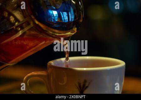 Le thé à la framboise est versé d'une théière en verre dans une tasse en céramique blanche. Odessa, Ukraine Banque D'Images