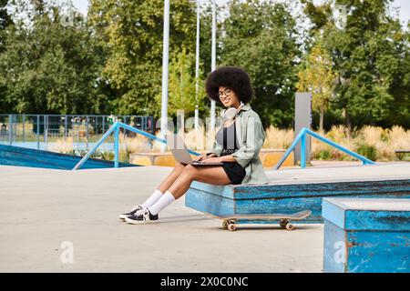 Une femme aux cheveux bouclés est assise sur un banc, tapant sur un ordinateur portable à l'extérieur dans un cadre urbain dynamique. Banque D'Images