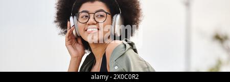 Une jeune femme en veste écoute de la musique à travers des écouteurs tout en incarnant le rythme dans un cadre urbain. Banque D'Images