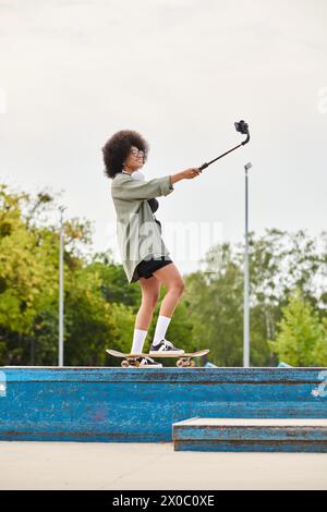 Une jeune femme afro-américaine aux cheveux bouclés glisse en douceur sur une rampe de skateboard dans un skate Park en plein air. Banque D'Images