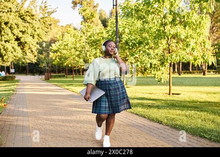 Une femme afro-américaine de grande taille en tenue décontractée marche sur un trottoir, un jour d'été. Banque D'Images