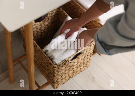 Femme mettant des serviettes dans le panier de rangement à l'intérieur, gros plan Banque D'Images