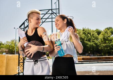 Deux jeunes femmes, amies et athlètes, se tiennent confortablement côte à côte sur un terrain de basket-ball en plein air en été. Banque D'Images