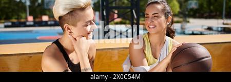 Deux jeunes femmes, amies, se relaxant après avoir joué au basket-ball en plein air, appréciant les uns les autres compagnie. Banque D'Images