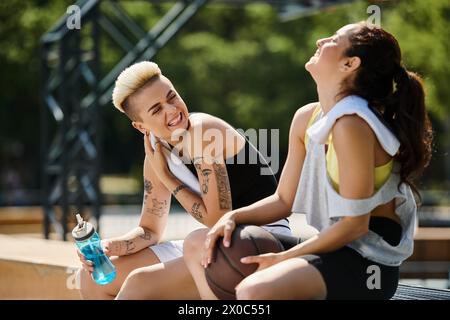 Deux jeunes femmes assises ensemble après avoir joué au basket-ball en plein air, profitant d'un moment d'amitié et de camaraderie. Banque D'Images