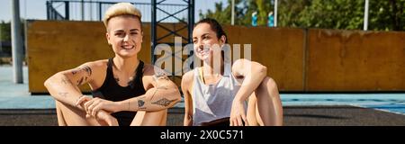 Deux jeunes femmes assises côte à côte, embrassant après avoir joué au basket-ball en plein air par une journée d'été ensoleillée. Banque D'Images