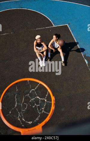 Une paire d'amies sportives assis au sommet d'un terrain de basket-ball extérieur par une journée ensoleillée. Banque D'Images