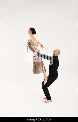 Jeune homme et jeune femme vêtus de noir exécutant des mouvements de danse acrobatique sur un sol blanc dans un cadre de studio. Banque D'Images