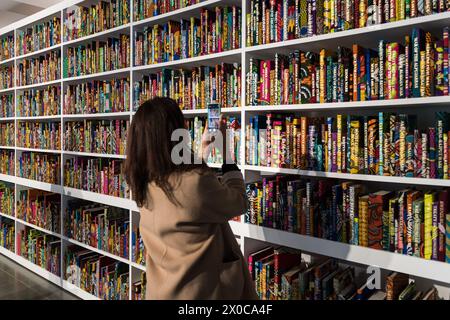 LONDRES, ROYAUME-UNI - 11 AVRIL 2024 : un visiteur prend une photo de la nouvelle installation à grande échelle intitulée «War Library» (2024), composée de 5 000 livres reliés en cire néerlandaise représentant des conflits et des traités de paix lors d'un appel photo pour l'exposition «Suspended States» de Yinka Shonibare à Serpentine South à Londres, au Royaume-Uni, le 11 avril 2024. La première exposition personnelle du travail de Shonibare dans une institution publique londonienne depuis plus de 20 ans explore les thèmes centraux des héritages du pouvoir colonial, des lieux de refuge et d’abri ainsi que l’impact écologique de la colonisation, la branche européenne Banque D'Images