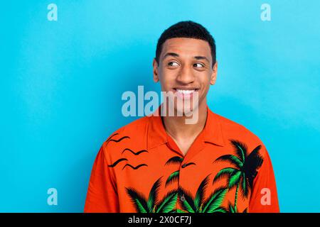 Photo de bonne humeur Dreamy Guy chemise imprimée habillée souriante regardant l'espace emtpy isolé fond de couleur bleue Banque D'Images