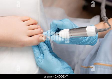 Maître de pédicure dans des gants en caoutchouc faisant de la pédicure quincaillerie à l'aide d'une perceuse à ongles pour femme. Banque D'Images