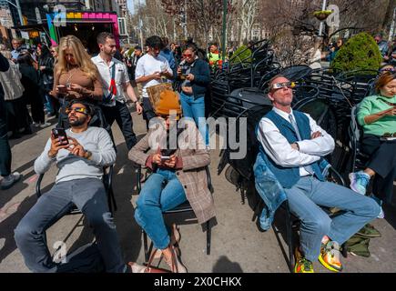 Des centaines de personnes se rassemblent à Flatiron Plaza à New York pour une fête d'observation à regarder, portant leurs lunettes de protection, l'éclipse solaire le lundi 8 avril 2024. New York City n'était pas sur le chemin de la totalité avec la lune couvrant 89% du soleil pendant la fenêtre de 15h15 à 15H30. (© Richard B. Levine) Banque D'Images