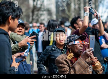 Des centaines de personnes se rassemblent à Flatiron Plaza à New York pour une fête d'observation à regarder, portant leurs lunettes de protection, l'éclipse solaire le lundi 8 avril 2024. New York City n'était pas sur le chemin de la totalité avec la lune couvrant 89% du soleil pendant la fenêtre de 15h15 à 15H30. (© Richard B. Levine) Banque D'Images