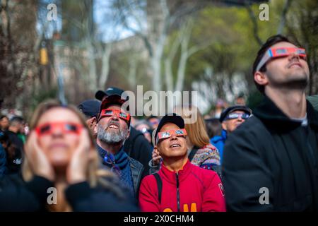 Des centaines de personnes se rassemblent à Flatiron Plaza à New York pour une fête d'observation à regarder, portant leurs lunettes de protection, l'éclipse solaire le lundi 8 avril 2024. New York City n'était pas sur le chemin de la totalité avec la lune couvrant 89% du soleil pendant la fenêtre de 15h15 à 15H30. (© Richard B. Levine) Banque D'Images