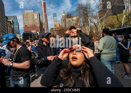 Des centaines de personnes se rassemblent à Flatiron Plaza à New York pour une fête d'observation à regarder, portant leurs lunettes de protection, l'éclipse solaire le lundi 8 avril 2024. New York City n'était pas sur le chemin de la totalité avec la lune couvrant 89% du soleil pendant la fenêtre de 15h15 à 15H30. (© Richard B. Levine) Banque D'Images