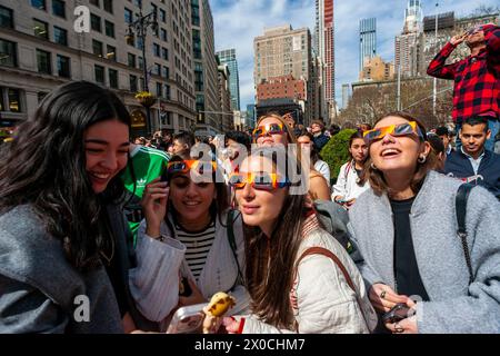 Des centaines de personnes se rassemblent à Flatiron Plaza à New York pour une fête d'observation à regarder, portant leurs lunettes de protection, l'éclipse solaire le lundi 8 avril 2024. New York City n'était pas sur le chemin de la totalité avec la lune couvrant 89% du soleil pendant la fenêtre de 15h15 à 15H30. (© Richard B. Levine) Banque D'Images