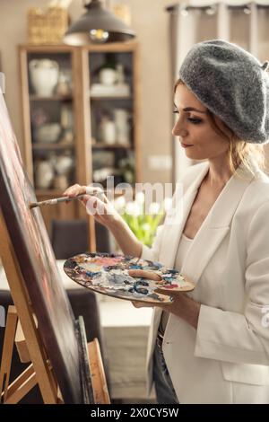 Belle peintre féminine appréciant tout en peignant dans le studio d'art à la maison. Femme artiste travaille sur la peinture acrylique abstraite dans le studio d'art. Banque D'Images
