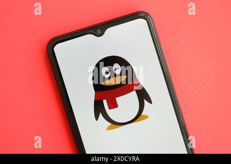 KIEV, UKRAINE - AVRIL 1, 2024 icône Tencent QQ sur l'écran du smartphone sur la table rouge gros plan. Écran iPhone avec logo APP sur fond rouge vif Banque D'Images