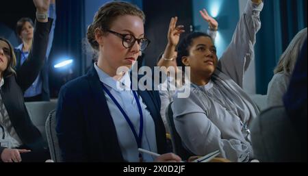 Journaliste féminine pose des questions, écrit la réponse d'un activiste ou d'un politicien lors d'une conférence de presse. Divers représentants des médias lèvent la main assis dans le bâtiment du gouvernement pendant l'entrevue. Banque D'Images