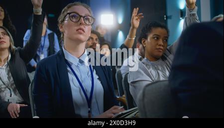 Journaliste féminine pose des questions, écrit la réponse d'un activiste ou d'un politicien lors d'une conférence de presse. Divers représentants des médias lèvent la main assis dans le bâtiment du gouvernement pendant l'entrevue. Banque D'Images