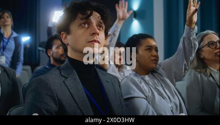 Un jeune homme représentant des médias pose des questions et écrit la réponse d'un politicien pendant la campagne de presse. Divers journalistes lèvent la main dans la salle de conférence du bâtiment du gouvernement. Banque D'Images