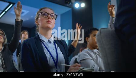 Les travailleurs de la presse multiethniques lèvent la main assise dans le bâtiment du gouvernement. Journaliste féminine pose des questions et écoute la réponse du représentant de l'organisation ou de l'homme politique pendant la conférence de presse. Banque D'Images