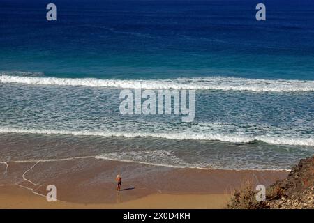 Homme solitaire debout dans des vagues peu profondes sur une plage de sable, El Cotillo, Fuerteventura. Prise en février 2024 Banque D'Images