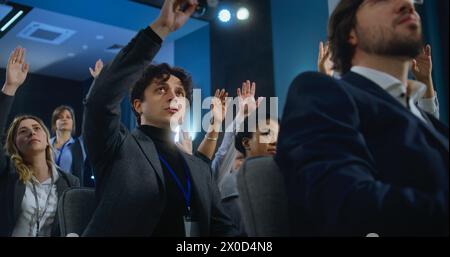 Les travailleurs de la presse multiethniques lèvent la main assise dans la salle de conférence du bâtiment du gouvernement. Un jeune journaliste masculin pose des questions, écoute les réponses ou les discours des activistes ou des politiciens pendant la campagne de presse. Banque D'Images