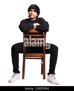 Un homme est assis sur une chaise en bois, les bras croisés. Il porte une chemise noire et un pantalon noir. La chaise est brune et a des lattes en bois. Le ma Banque D'Images