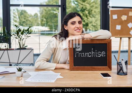 Une femme d'affaires est assise à un bureau moderne, affichant en évidence un signe comme symbole de ses efforts entrepreneuriaux. Banque D'Images