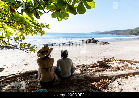Mère et fils, touristes, détente, assis à l'ombre sur une plage Playa Montezuma près du village Montezuma par une belle journée ensoleillée d'été, Costa rica Banque D'Images