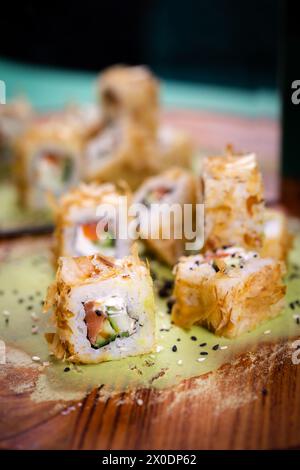 Délicieux rouleau de sushi frit avec saumon frais, concombre, sur assiette en bois avec wasabi et graines de sésame, un délice japonais. Banque D'Images