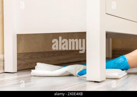 la femme au foyer portant des gants lave le sol sous le placard. nettoyage humide du sol dans la chambre. nettoyage de la poussière sous les armoires. Photo de haute qualité Banque D'Images