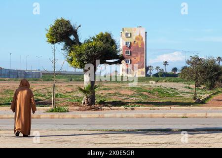 Casablanca, Maroc - 20 janvier 2019 : homme marocain dans djellabah marchant vers un bâtiment dans le quartier d'El Hank décoré d'une fresque murale par un artiste de rue Banque D'Images