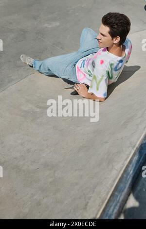 Un homme en tenue décontractée se prélassant sur le sol à côté de son skateboard, profitant d'un moment de détente dans un cadre urbain dynamique. Banque D'Images