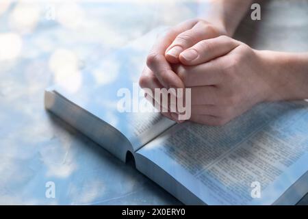 Religion. Double exposition de ciel et femme chrétienne priant sur la Bible à table, gros plan. Effet bokeh Banque D'Images