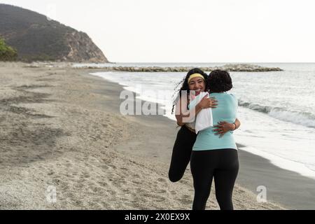 Deux femmes s'embrassent joyeusement sur une plage tranquille, les vagues lançant doucement le rivage. Banque D'Images