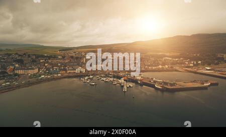 Pier Town citycsape avec des bâtiments historiques à Ocean Bay Aerial. Soleil brille sur les navires, les yachts au quai de la marina. Rues, route avec voitures, camions. Colline verte, vallée à Campbeltown City, Écosse, Europe Banque D'Images