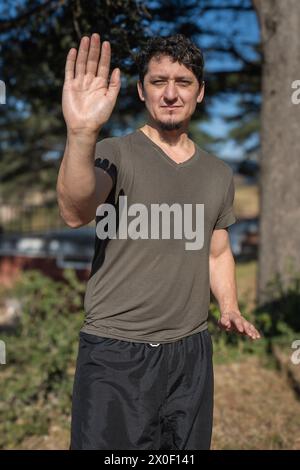 Au crépuscule, un homme s’immerge dans la pratique du Chi Kung, les pieds fermement plantés sur le sol, sa posture reflétant l’équilibre et l’harmonie. Banque D'Images