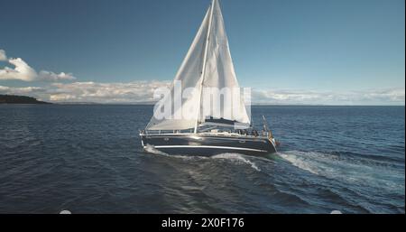 Gros plan au ralenti du yacht de luxe à voile à Ocean Bay Aerial. Course de bateaux en pleine mer. Régate de voilier au port de Brodick, île d'Arran, Écosse, Europe. Paysage marin avec reflet du soleil lors de la croisière estivale Banque D'Images