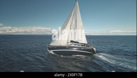 Gros plan au ralenti du yacht de luxe à voile à Ocean Bay Aerial. Course de bateaux en pleine mer. Régate de voilier au port de Brodick, île d'Arran, Écosse, Europe. Paysage marin avec reflet du soleil lors de la croisière estivale Banque D'Images