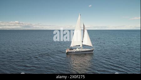 Réflexion d'un bateau à voile au ralenti sur l'antenne de la baie maritime. Gros plan voilier au golfe de l'océan. Course de croisière de yacht de passagers à l'été. Sunlight Seascape au port de Brodick, Écosse, Europe Banque D'Images